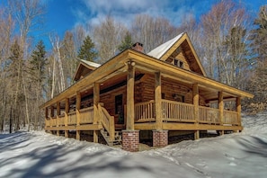 Eine Blockhütte mit Veranda, umgeben von Schnee und Bäumen.