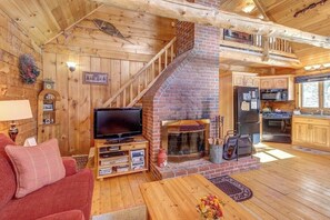 Ein gemütliches Blockhaus mit Kamin, Holzwänden, Fernseher und Küchenzeile.