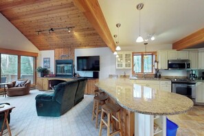 A spacious kitchen with a large island, wooden ceiling, and a television. - Bright, Open Home with Wraparound Deck & Mountain Views - 2 Miles to Skiing (Ludlow)