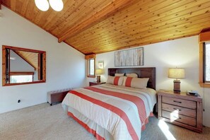 A bedroom with a wooden ceiling, a large bed with a striped bedspread, a nightstand with a lamp, and a wooden dresser. - Bright, Open Home with Wraparound Deck & Mountain Views - 2 Miles to Skiing (Ludlow)
