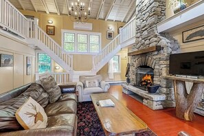 Ein geräumiges Wohnzimmer mit Kamin aus Stein, einer Ledersofa, einem Holztisch und einer Treppe, die in ein Obergeschoss führt.