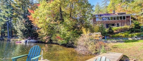 A lakeside cabin with a dock and chairs, surrounded by trees and a clear view of the water.