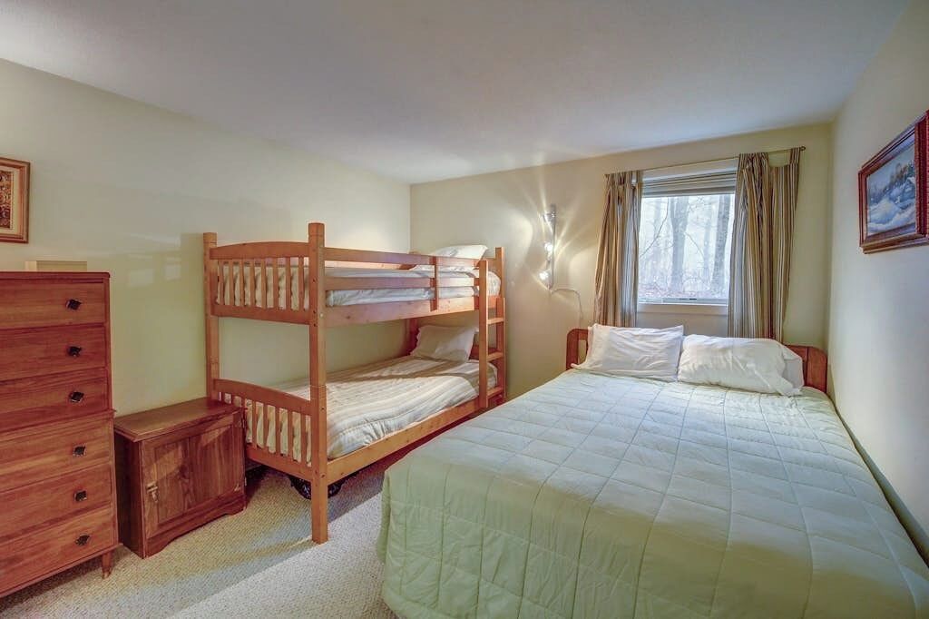 A bunk bed room with a dresser, a small cabinet, and a window with curtains.