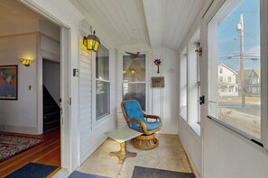 A sunroom with a wicker chair, a small table, and a view of the outside. - Charming home close to skiing & golf, wifi, piano, w/d, soaker tub (Ludlow)