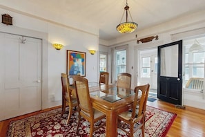 A dining area with a glass table, wooden chairs, a red patterned rug, a chandelier, and a painting on the wall. - Charming home close to skiing & golf, wifi, piano, w/d, soaker tub (Ludlow)