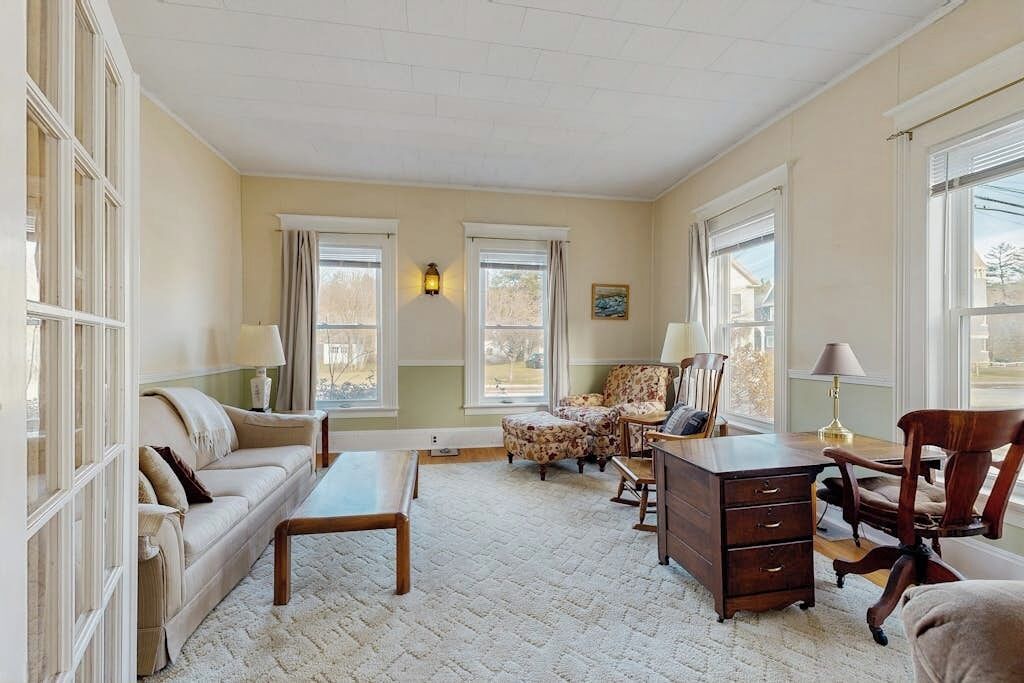 A spacious living room with a sofa, armchairs, a coffee table, and a wooden desk.