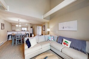 A living room with a sectional sofa, a dining area with a table and chairs, and a kitchen in the background. - Two Okemo condos - ski-in/ski-out - pool, fast WiFi, washer/dryer (Ludlow)