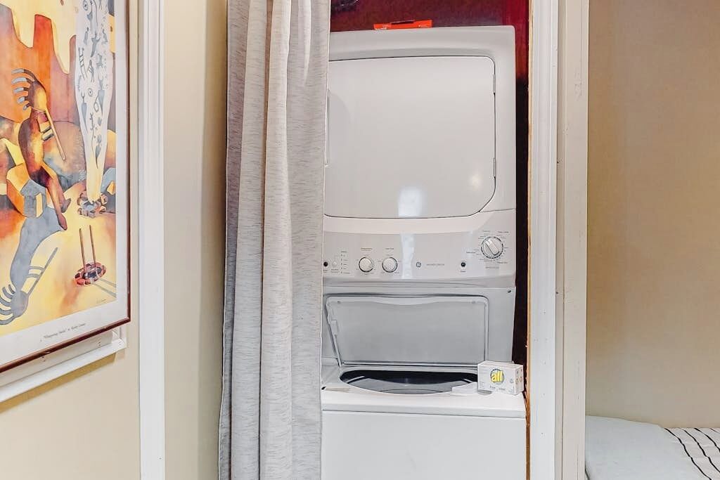 A laundry room with a washing machine and dryer, a framed artwork on the wall, and a curtain.