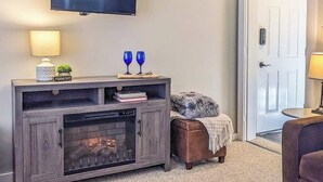Una sala de estar con chimenea, un televisor montado en la pared y una puerta a la derecha.