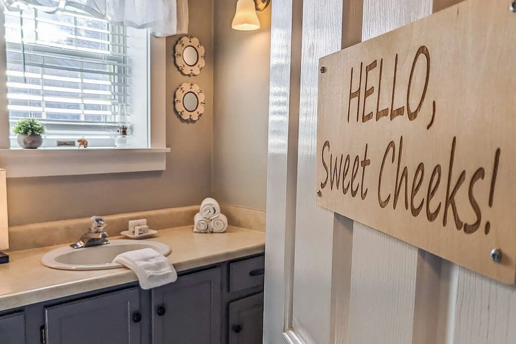 Une salle de bain avec un lavabo, une serviette et un panneau sur lequel on peut lire : « BONJOUR, jolies fesses ! »