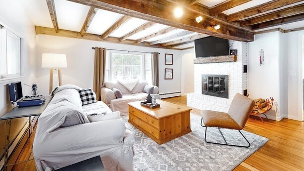 Ein modernes Wohnzimmer mit freiliegenden Holzbalken, einem Kamin, einer Couch, einem Couchtisch und einem Sessel.