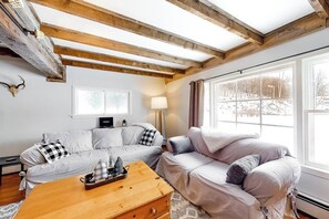 Ein gemütliches Wohnzimmer mit einer Couch, einem Holztisch und einem Fenster mit Blick auf Bäume.