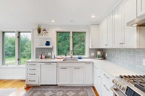 A modern kitchen with white cabinetry, a large window, and a built-in stove.