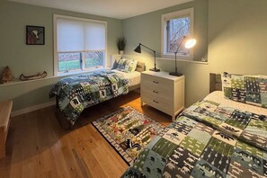 A bedroom with two beds, a nightstand, a lamp, a window with blinds, and a rug. - Tranquil house w/ pond, 3-hole golf course, sandy beach, bbq, firepit, & trails (Londonderry)