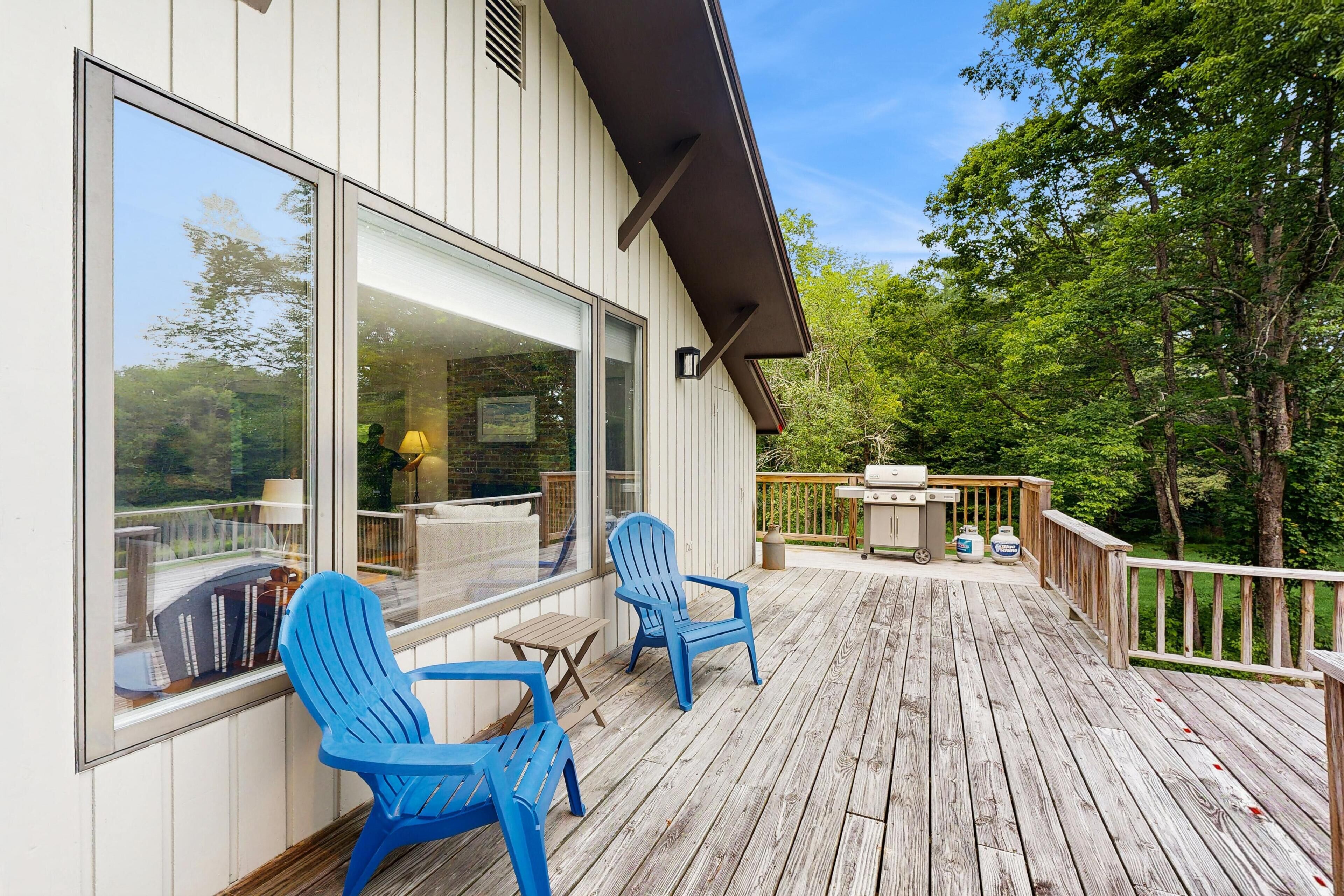 A wooden deck with two blue chairs, a small table, and a barbecue grill.