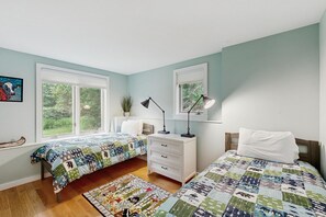A bedroom with two beds, a nightstand, a desk, and a window.