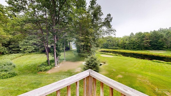 Campo de golf con una terraza de madera al frente, rodeado de exuberante vegetación y árboles.