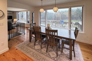 A dining area with a wooden table and chairs, large windows, and a view of the outdoors. - Tranquil house w/ pond, 3-hole golf course, sandy beach, bbq, firepit, & trails (Londonderry)