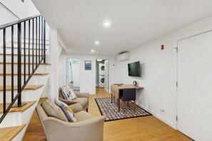A modern apartment with a staircase, a sofa, a desk, and a television.