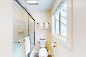 Ein Badezimmer mit Duschkabine aus Glas, Toilette und Fenster.