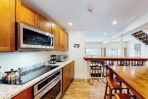 Cocina con armarios de madera, microondas, horno, encimera de granito y barra con taburetes.