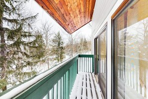 Un balcón con techo de madera, baranda verde y vistas a árboles cubiertos de nieve.