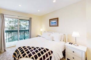 Ein Hotelzimmer mit Bett, zwei Nachttischen, einem Fenster mit Vorhängen, einem gerahmten Bild an der Wand und Balkonblick.