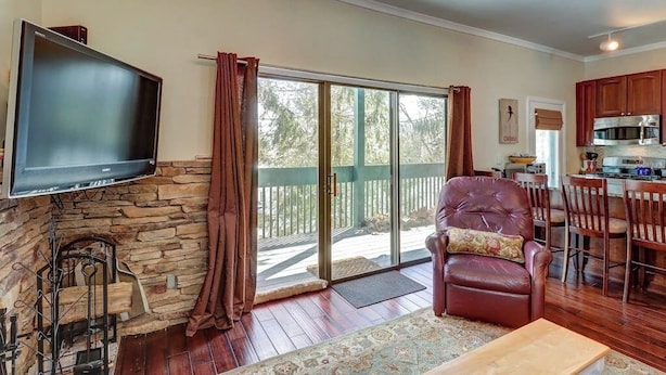 A living room with a stone fireplace, a flat-screen TV, a leather chair, a dining area with wooden chairs, and a kitchen with a microwave. - Renovated condo w/ shared tennis - walk to trail (Ludlow)