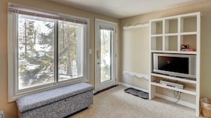 A room with a large sliding glass door, a bench, a TV on a white stand, and a view of trees outside. - Renovated condo w/ shared tennis - walk to trail (Ludlow)