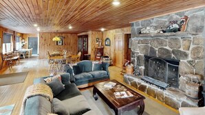 Ein gemütliches Wohnzimmer mit Kamin aus Stein, Holzboden und einem Essbereich mit Tisch und Stühlen.