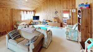 Ein gemütliches Zimmer mit Holzwänden, einem Fernseher, einer Couch, einem kleinen Tisch und einem Bücherregal.