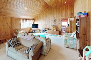 Una habitación acogedora con paredes de madera, televisión, sofá, una mesita y una estantería.