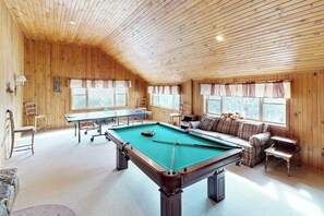 Un tavolo da biliardo in una stanza con pareti in legno e soffitto a sbalzo. Si intravede un divano e un tavolino sullo sfondo.