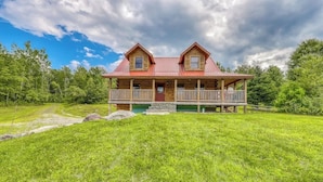 A two-story log cabin with a porch and a stone foundation.