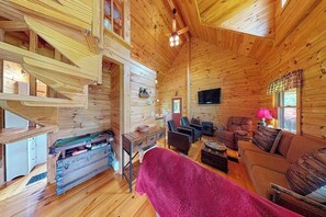 Interior de una cabaña de troncos con chimenea, zona de estar y televisor.