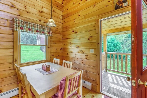Interior de una cabaña de madera con una mesa de comedor, sillas, una ventana y una puerta que da al exterior.
