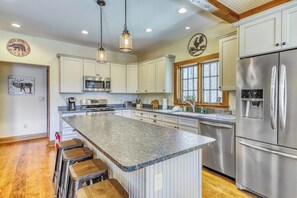 A kitchen with a large island, stainless steel appliances, and wooden bar stools. - Lakefront home with amazing views, fireplace, firepit, & gas grill (Ludlow)
