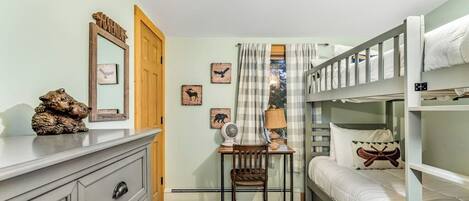 A bunk bed room with a desk, chair, and a dresser.