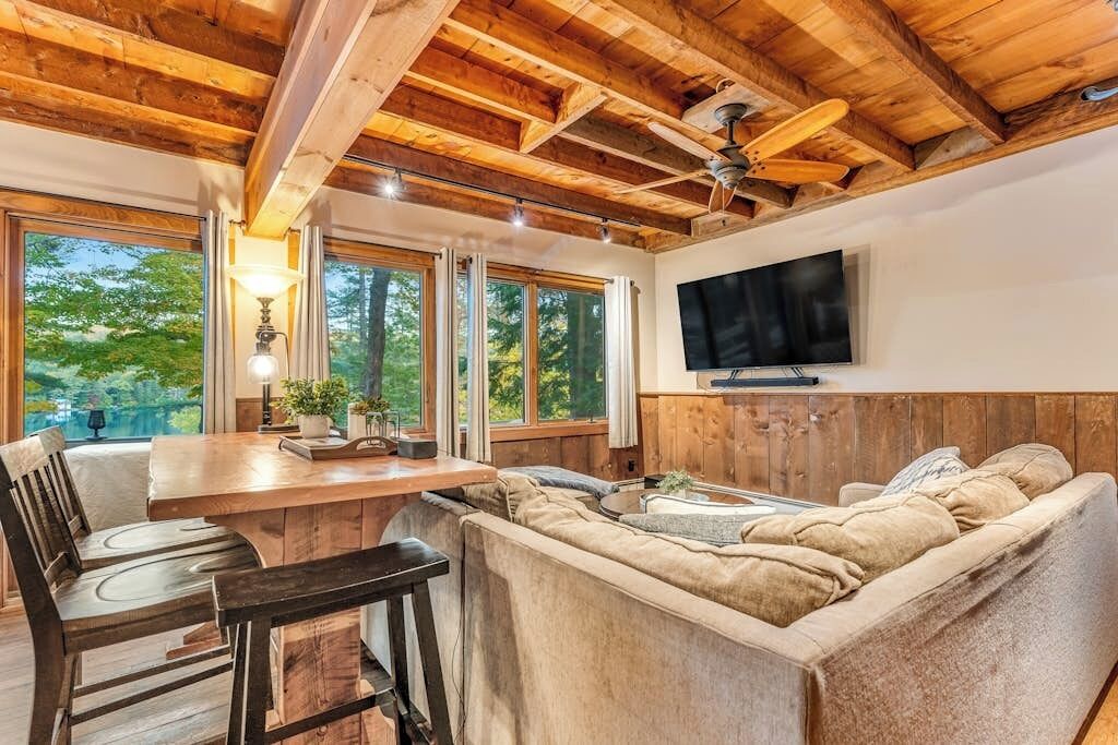 Un intérieur en bois comprenant un coin repas, un canapé, une télévision et de grandes fenêtres.
