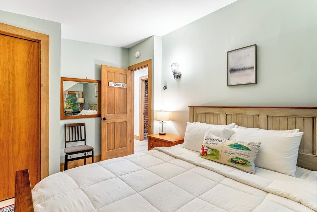 Une chambre à coucher comprenant un lit, une table de chevet, une lampe, un luminaire fixé au mur, un tableau encadré et une porte avec une pancarte.