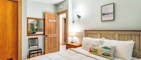 Une chambre à coucher comprenant un lit, une table de chevet, une lampe, un luminaire fixé au mur, un tableau encadré et une porte avec une pancarte.