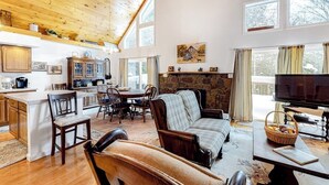 A spacious living area with a stone fireplace, wooden ceiling, and large windows. - Perfect Home Away near Town & Skiing w/ Private Gas Grill, Large Deck (Ludlow)