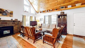 A cozy living room with a stone fireplace, wooden furniture, and a television. - Perfect Home Away near Town & Skiing w/ Private Gas Grill, Large Deck (Ludlow)