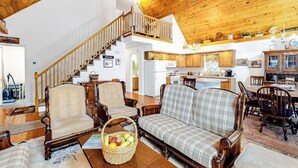 A spacious living room with a high wooden ceiling, a staircase leading to an upper level, a dining area with wooden chairs, and a kitchen area with wooden cabinets. - Perfect Home Away near Town & Skiing w/ Private Gas Grill, Large Deck (Ludlow)