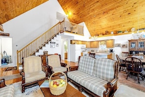 Ein geräumiges Wohnzimmer mit hohen Holzbalken, einer Treppe zu einer oberen Ebene, einem Essbereich mit Holzkästen und einer Küchenzeile mit Holzausstattung.