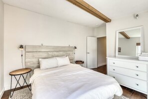 Ein Schlafzimmer mit einem Bett, einem hölzernen Kopfteil, einer weißen Kommode und einem Spiegel.