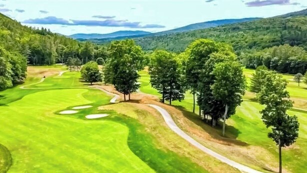 A golf course with a winding path, trees, and a distant mountain range.