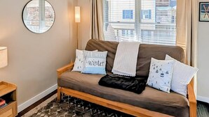 A cozy room with a brown sofa, a round mirror, and a view of buildings through the window.
