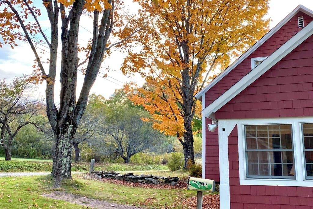 A red building with a white window, surrounded by trees with autumn leaves.