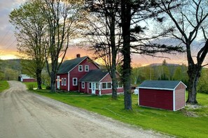 Ein rotes Haus mit Garage, umgeben von Bäumen und einer unbefestigten Straße.